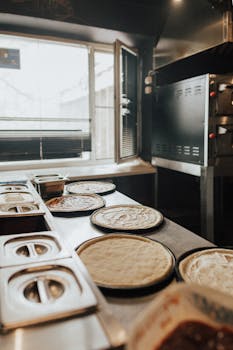 Pizza dough ready for toppings in a professional pizzeria kitchen setting.