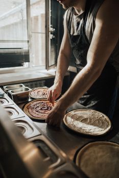 Artisan pizza preparation captured in a sunlit kitchen with focus on sauce application.