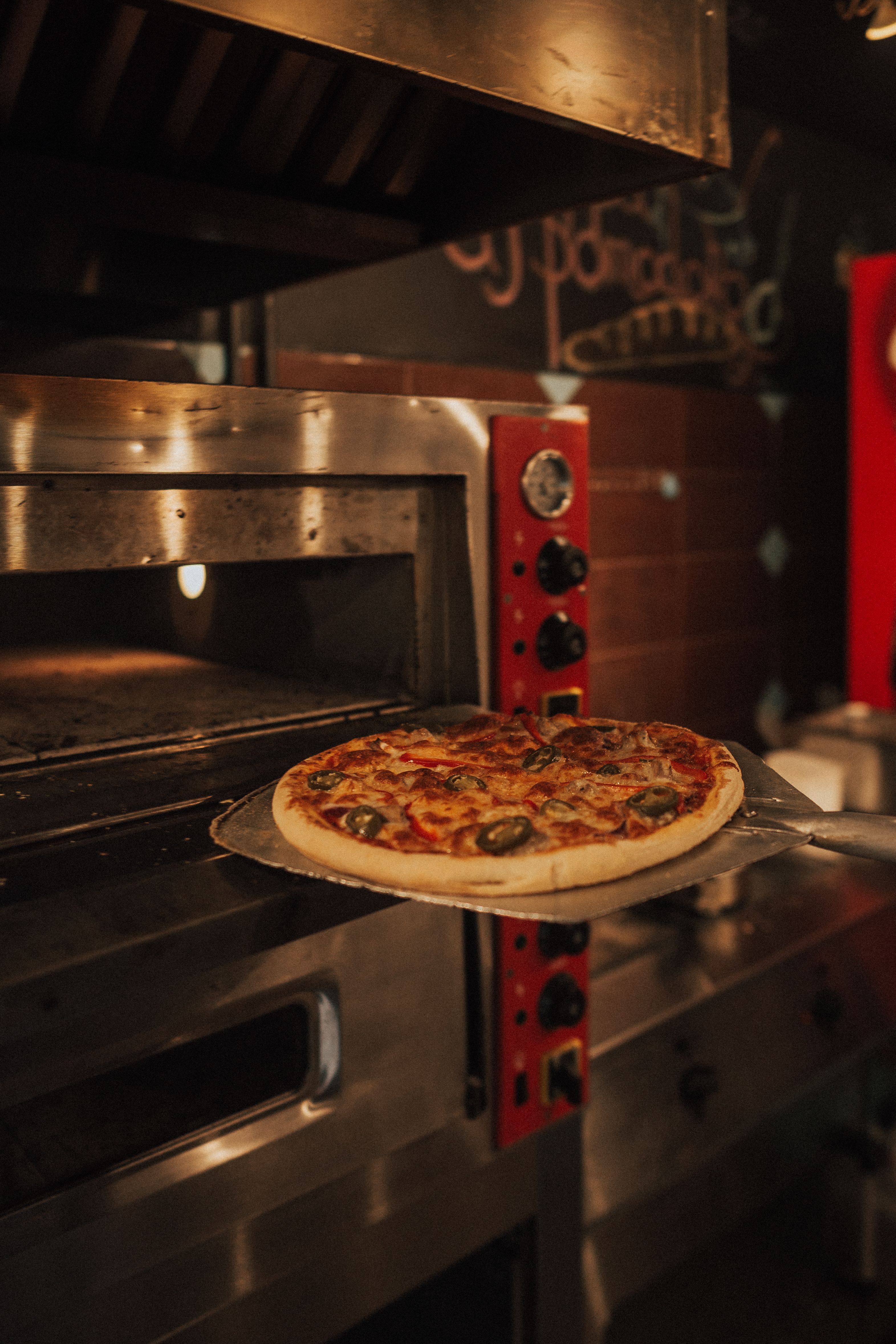 Close-up of a freshly baked pizza being taken out of a rustic oven in a cozy kitchen setting.