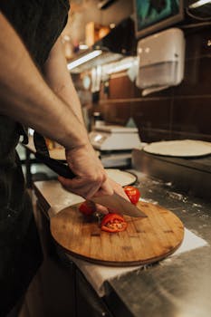 Close-up of chef slicing tomato on a wooden chopping board in a professional kitchen setting.
