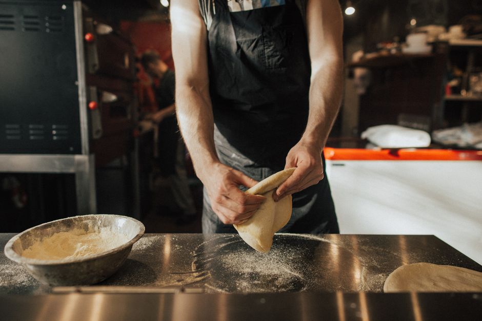 Close-up of a chef preparing pizza dough in a pizzeria kitchen.
