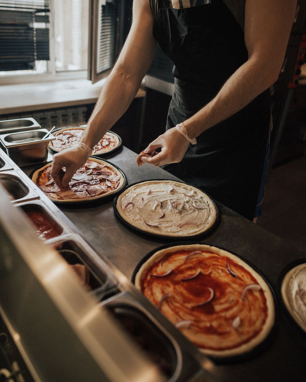 Hands in a plain apron preparing pizzas, close view