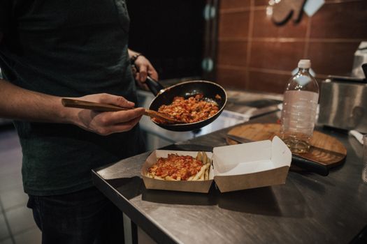 A person preparing a takeout meal with sauce in a frying pan on a kitchen counter.