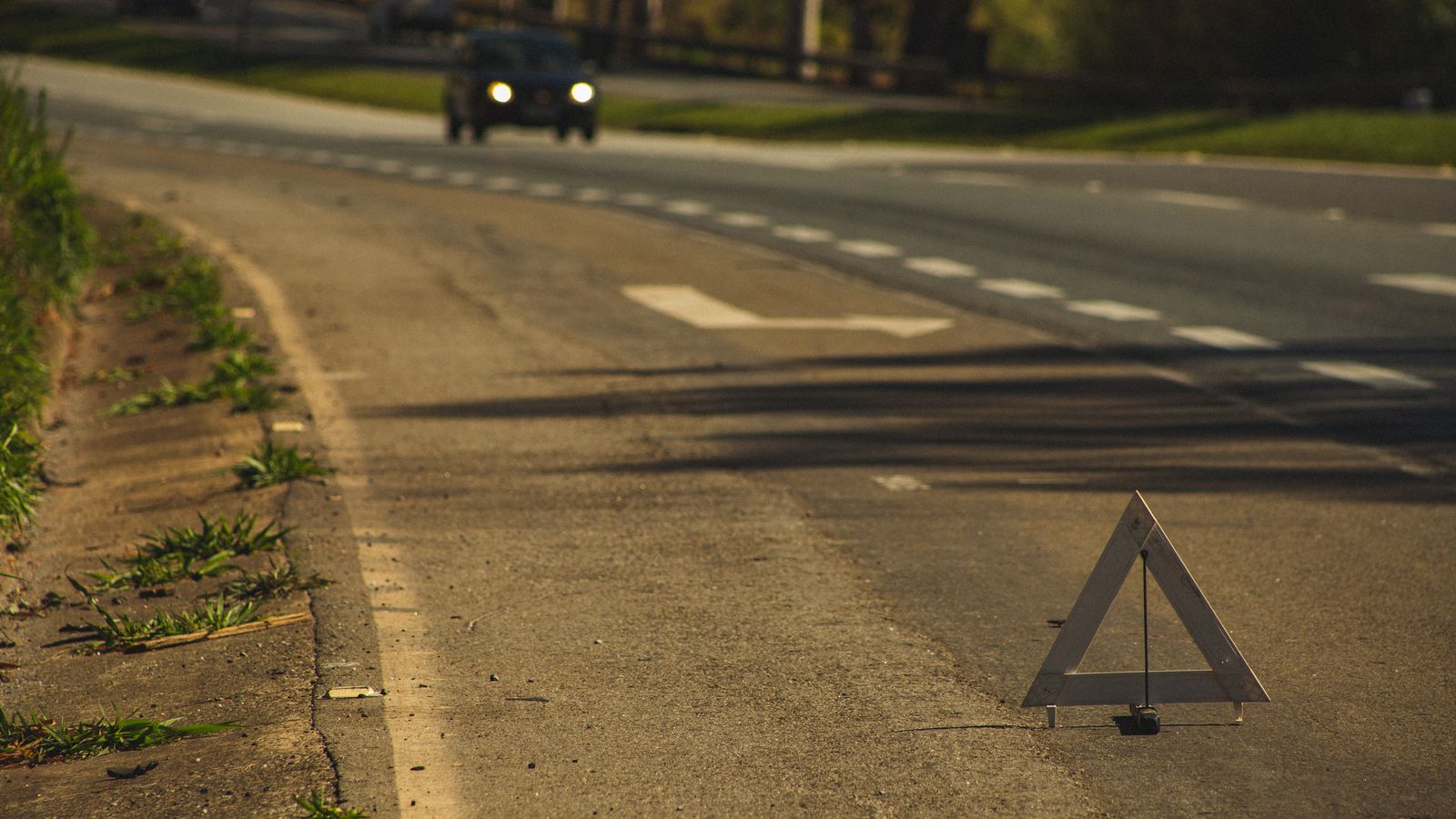 Automobile with headlights on driving on asphalt road with triangular sign in twilight
