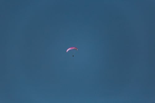 From below of unrecognizable traveler on paraglider soaring in blue sky in daylight