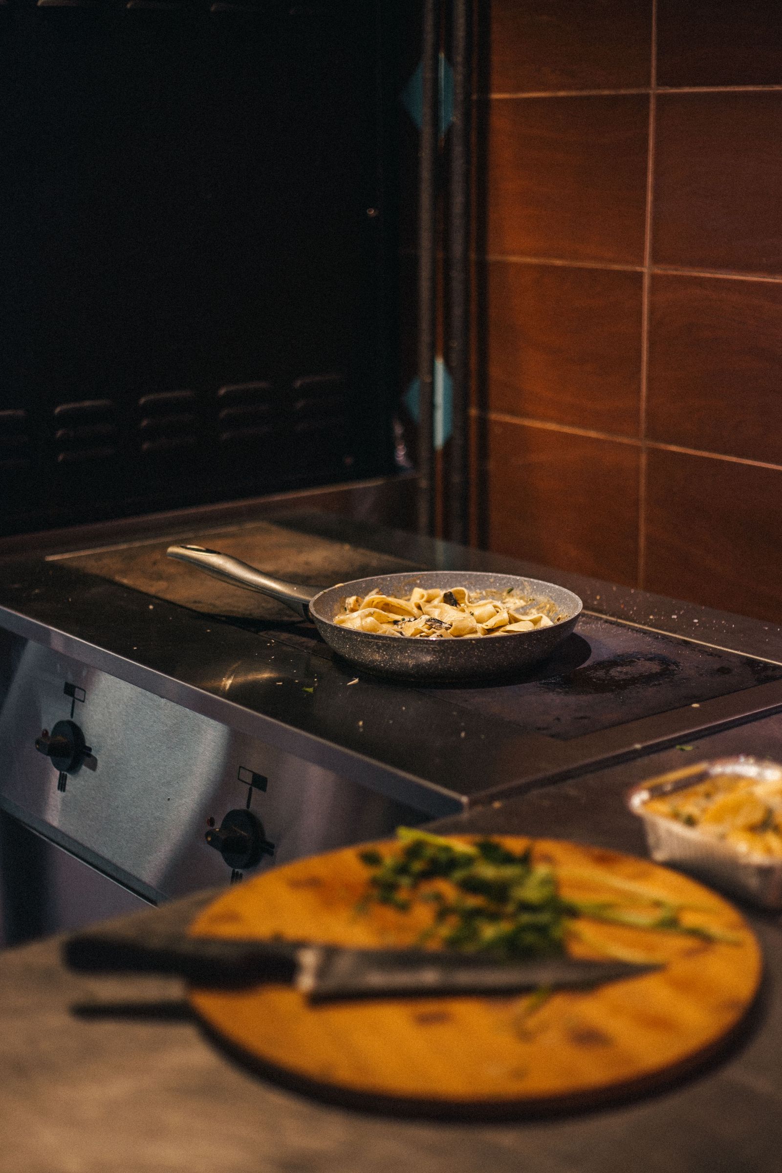 Close-up of a frying pan with pasta on a stove, capturing kitchen preparation scene.