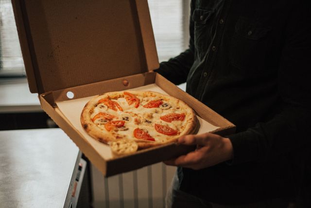 Personne tenant une boîte avec une pizza cuite, idéale pour une pizza à emporter à Bordeaux Caudéran