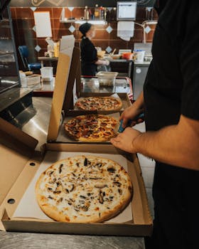 A chef cuts freshly baked pizzas ready for delivery in a busy restaurant kitchen.