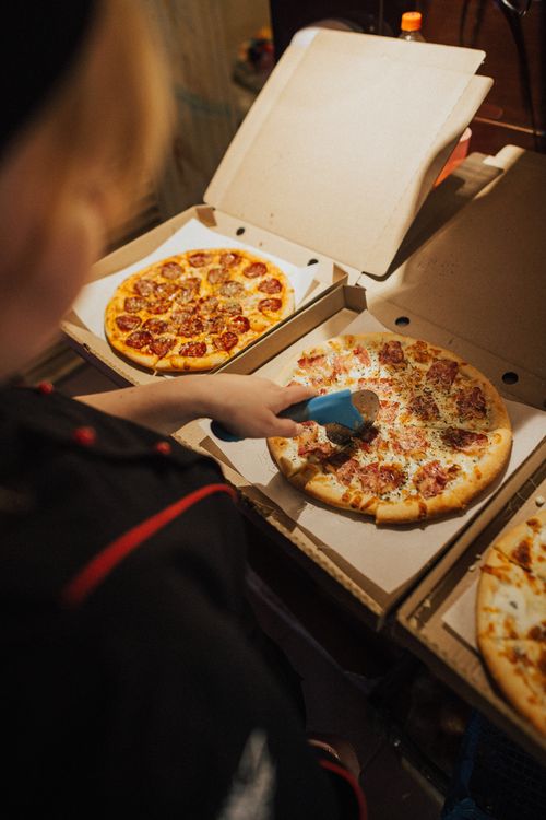 Free A person using a pizza cutter to slice pizzas inside open boxes, ready for delivery. Stock Photo
