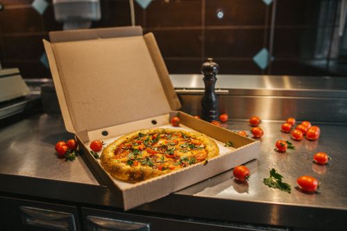 Free Open pizza box with fresh tomatoes on a kitchen counter, a perfect culinary scene. Stock Photo