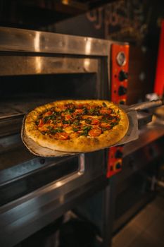 Delicious freshly baked pizza with vegetables being removed from the oven on a wooden peel.