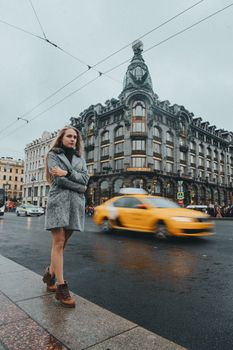 一名女子站在城市街道上，一辆模糊的黄色出租车驶过一座华丽的历史建筑