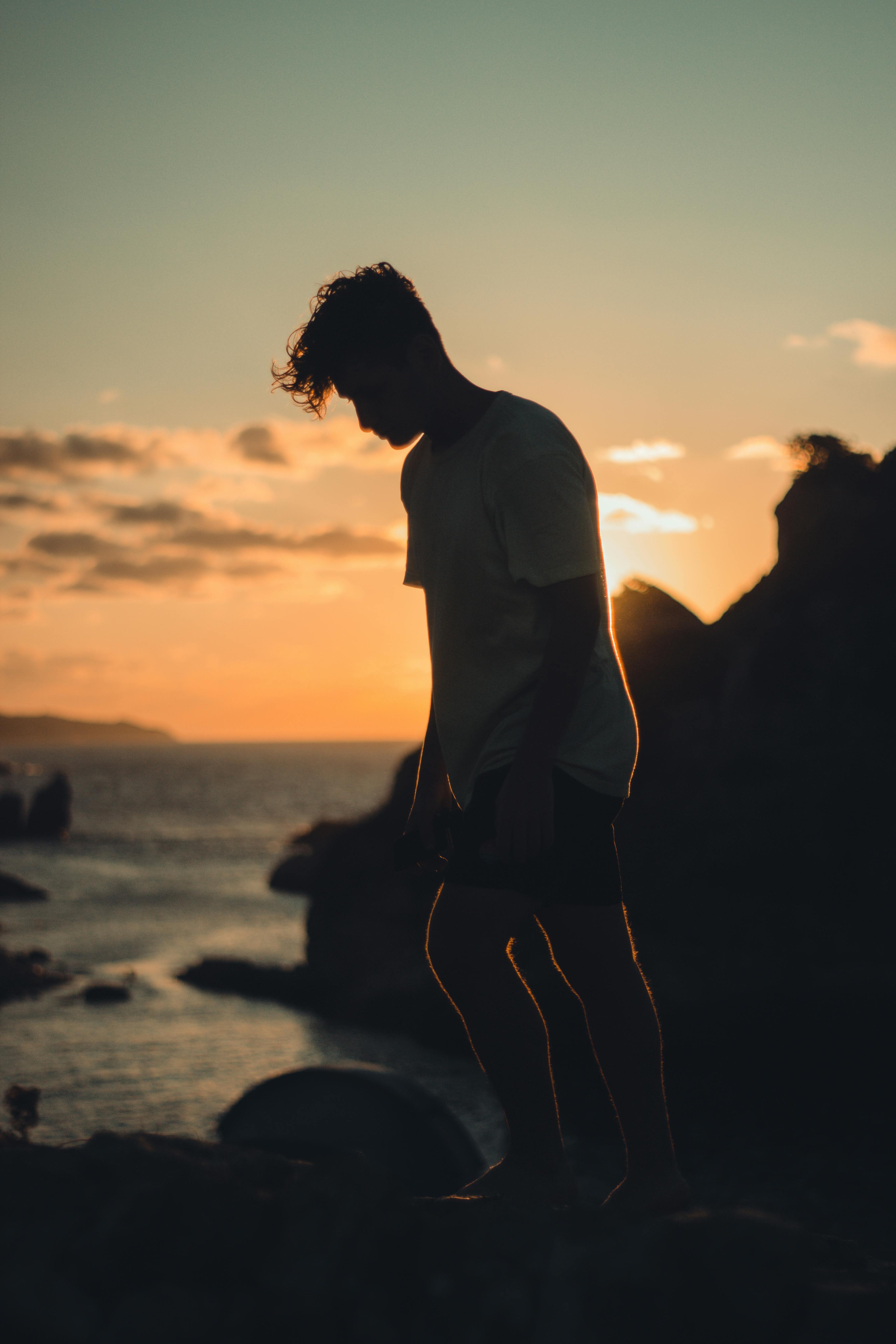 man in white t shirt standing on beach during sunset