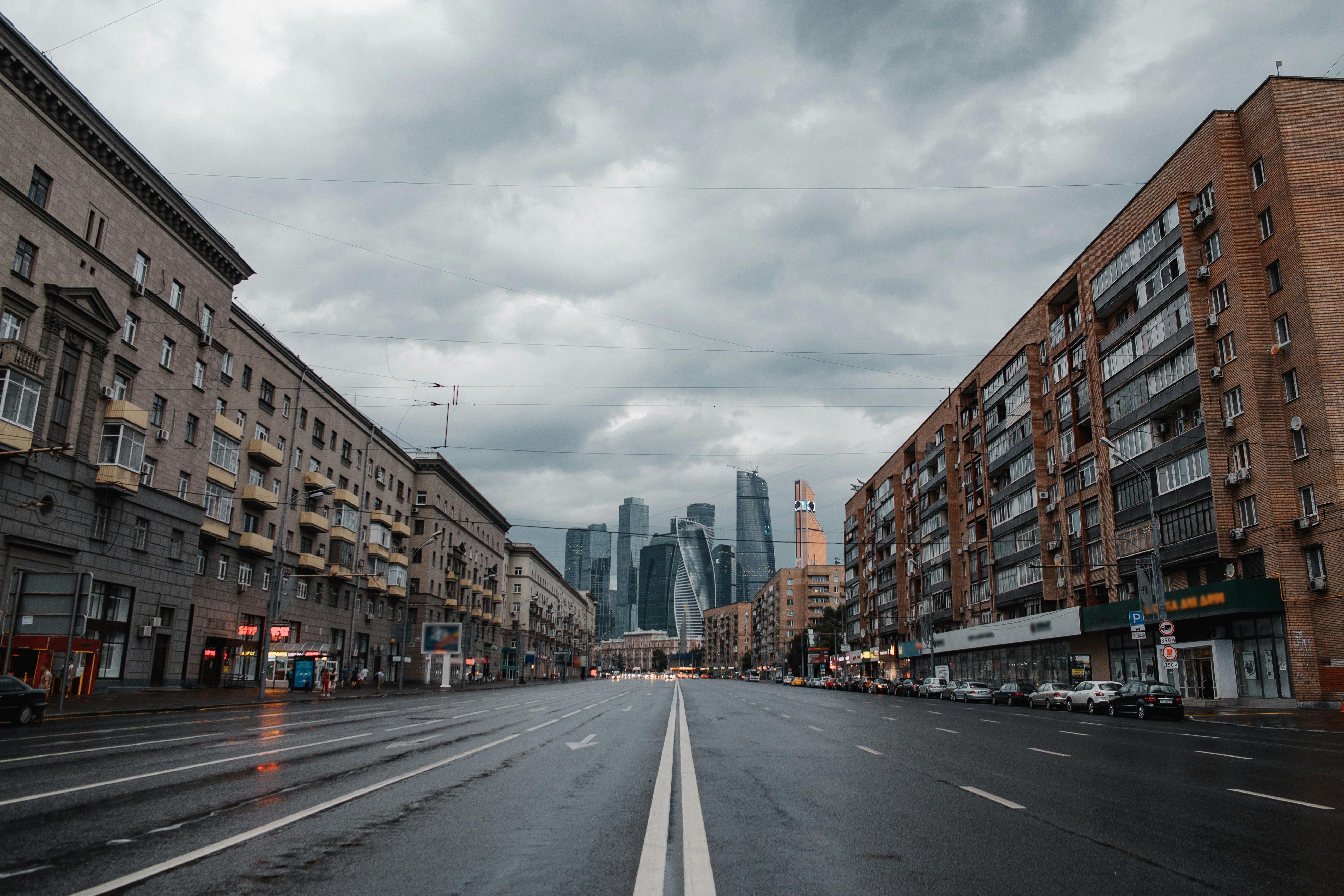 一条宽阔的街道两侧矗立着建筑物，在多云的天空下延伸向现代化的摩天大楼