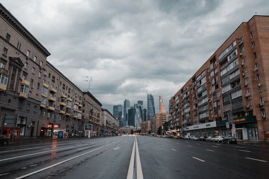 一条宽阔的街道两侧矗立着建筑物，在多云的天空下延伸向现代化的摩天大楼