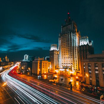 A bustling city street at night with an illuminated skyscraper and dynamic light trails.