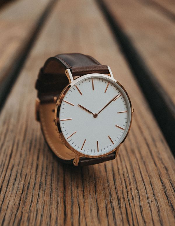 Minimalist analog watch with a brown leather strap on wood — photo by Max Avans on Pexels