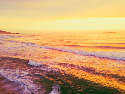 Free Spectacular scenery of foamy waves of powerful ocean rolling on sandy beach against picturesque bright sunset sky Stock Photo