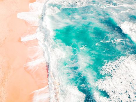 Stunning aerial shot showing turquoise waves crashing on sandy beach.