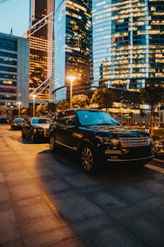 Elegant SUVs parked along illuminated city streets at dusk, reflecting modern urban architecture.