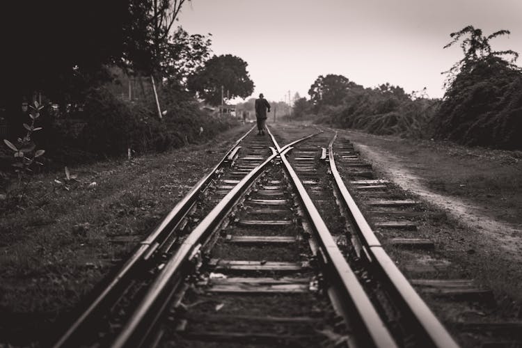 Grayscale Photo Of A Person Walking On Railway Track 