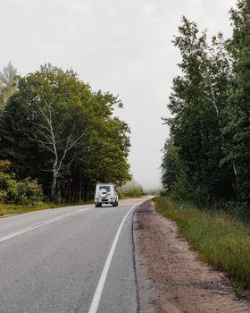 A white SUV driving down a lush, tree-lined country road.