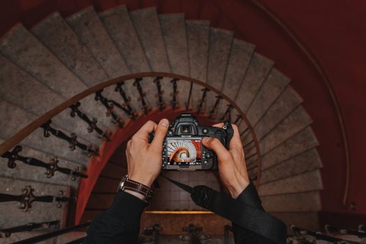 Hands holding a DSLR capturing an elegant spiral staircase from above.