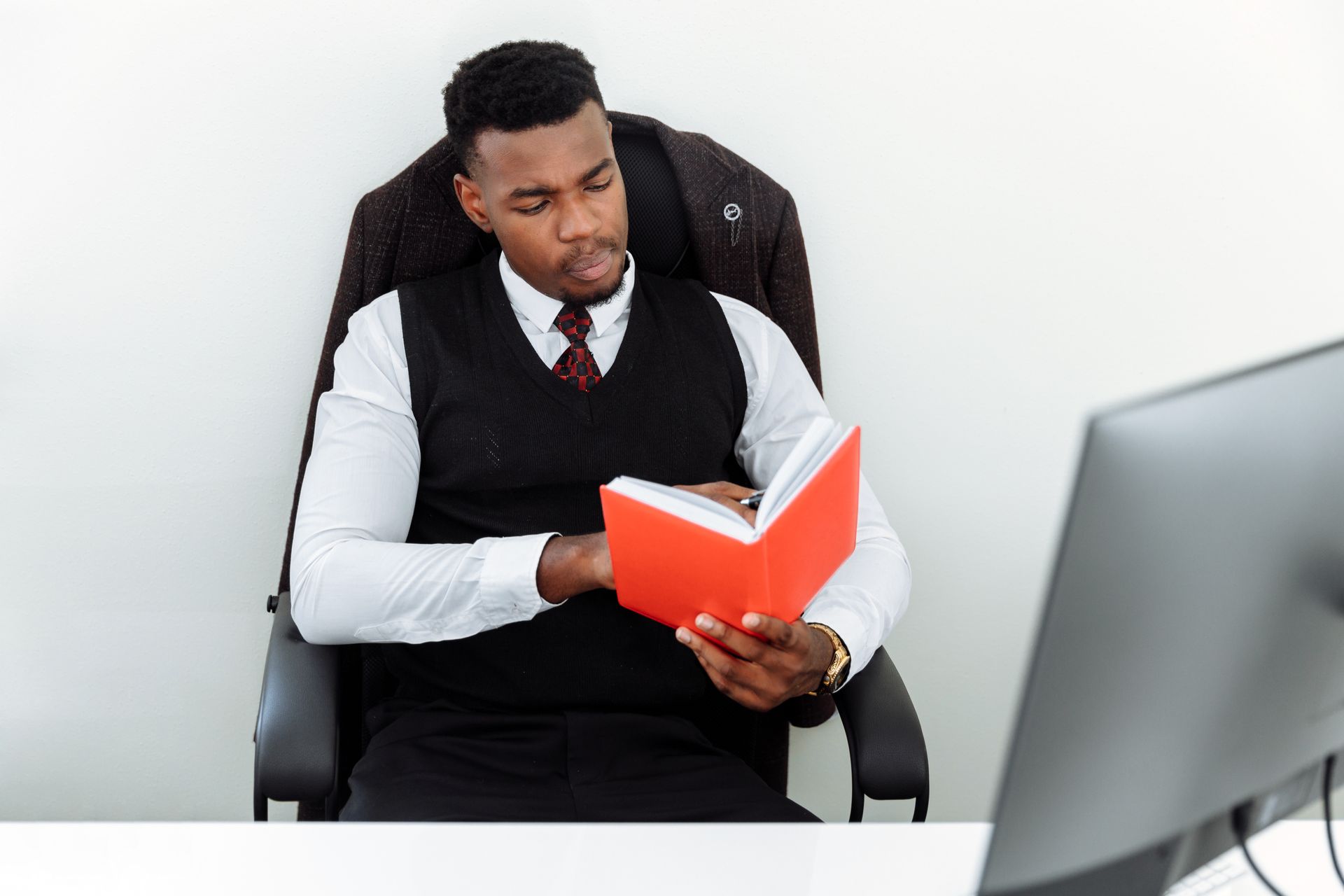 Focused African American man reading a red book at his workspace in an office setting.