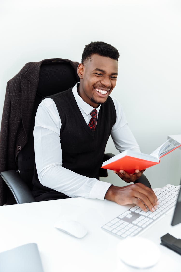 A Smiling Man Sitting While Holding A Notebook