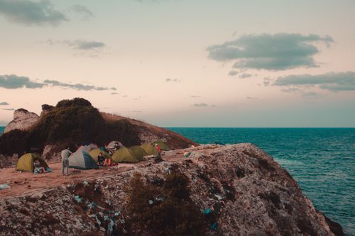 Free Scenic coastal camping on Turkish cliffs with tents, sea, and dramatic sky. Stock Photo
