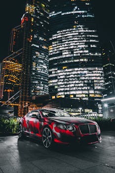 Red Bentley Continental GT parked against illuminated skyscrapers at night.