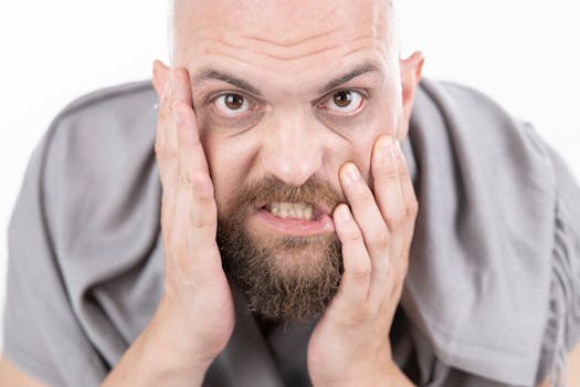 Close-up of a bearded man showing frustration with hands on face.