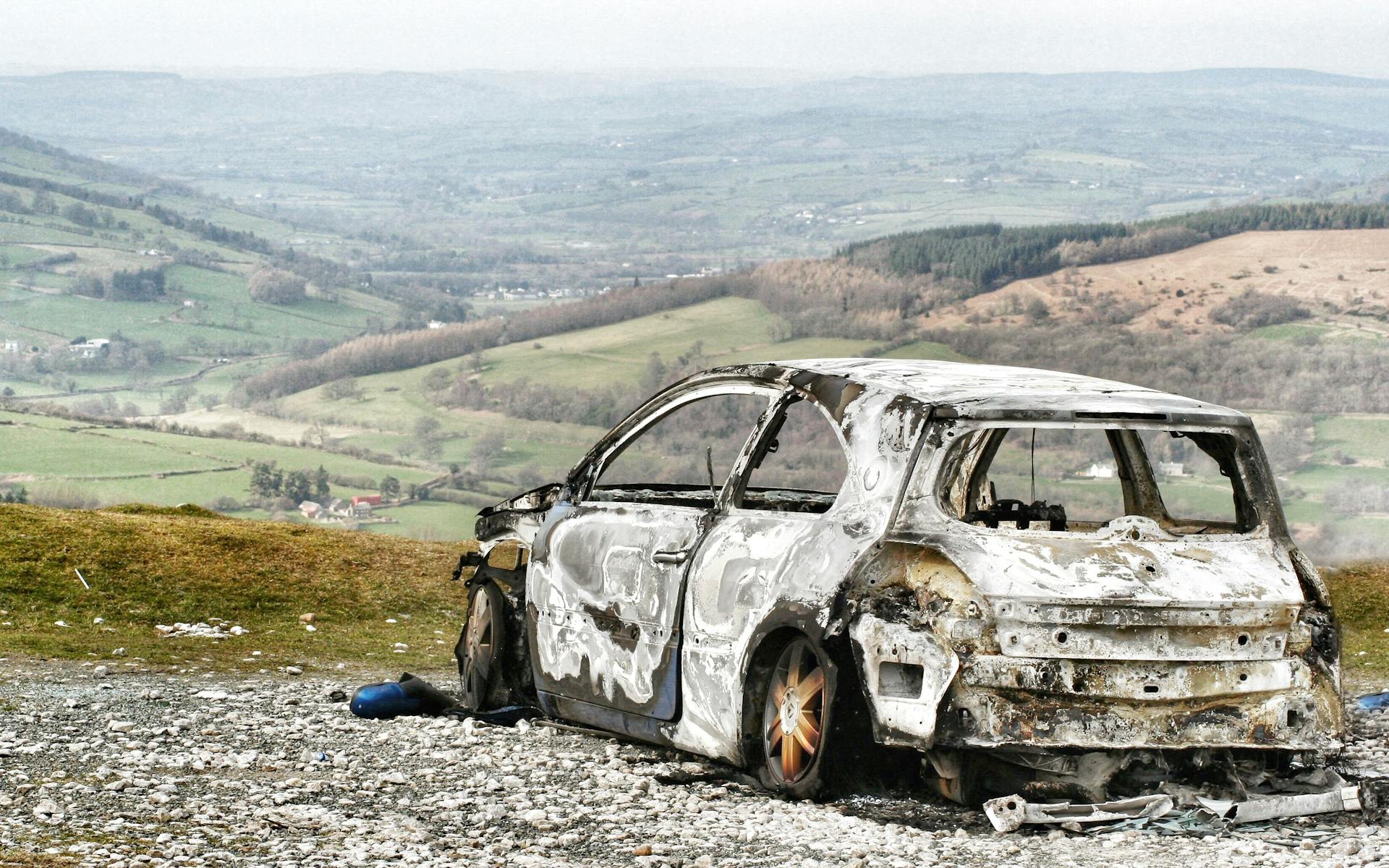 A burnt car wreck in a scenic rural landscape, depicting abandonment.