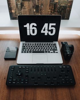 A contemporary workspace with a laptop, control panel, camera, and portable drive on a wooden desk.