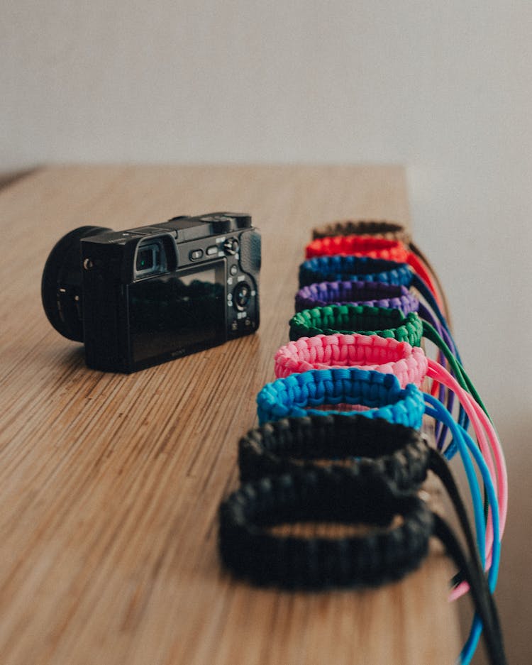 Black Camera Beside Colorful Camera Wrist Straps On Wooden Table