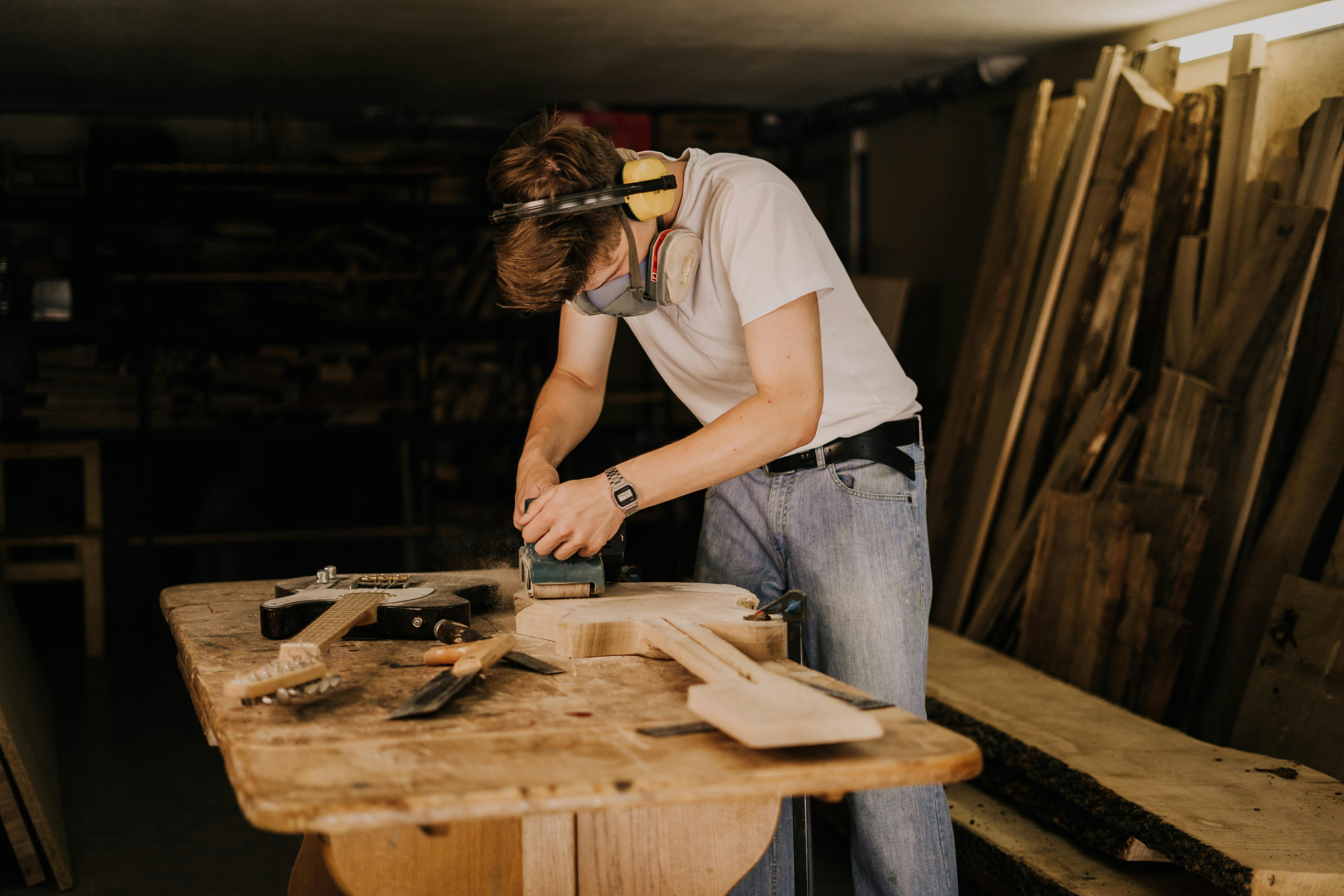 man grinding a wooden guitar in a workshop