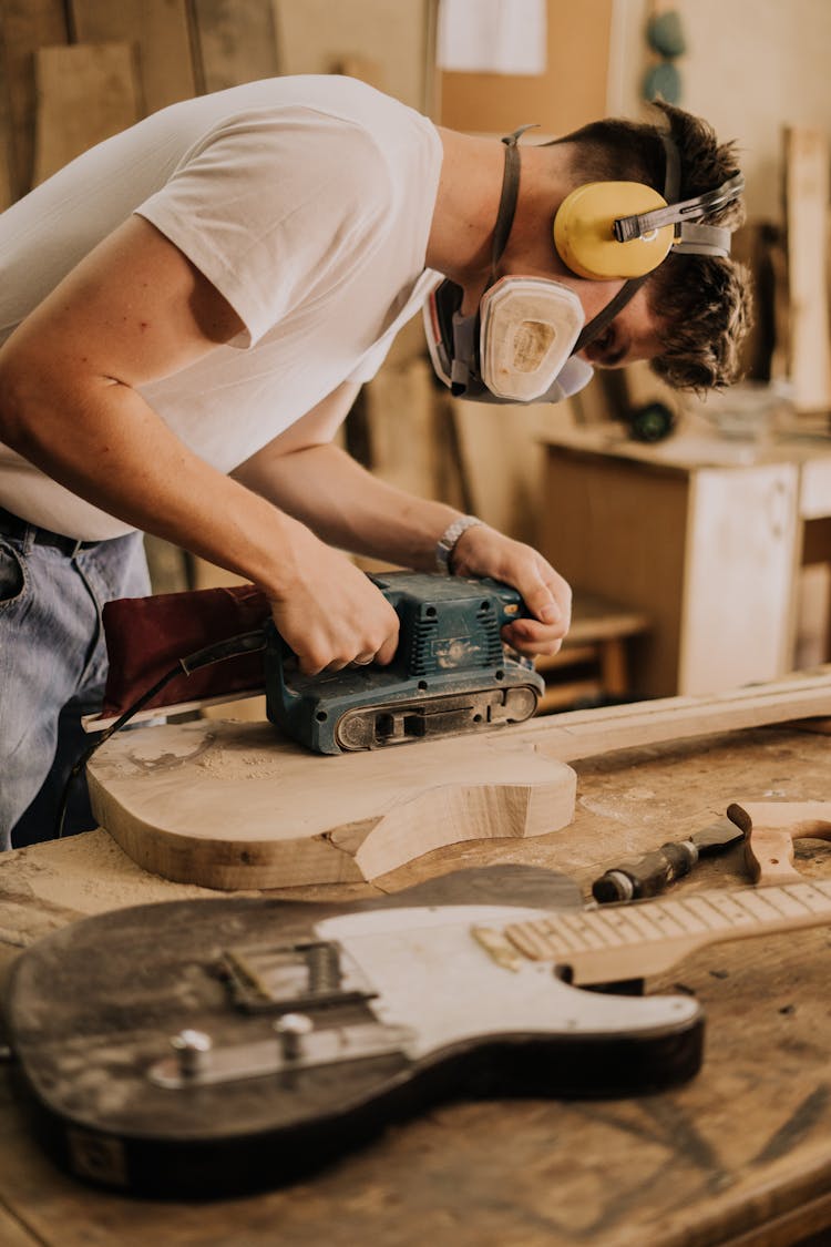 A Man Using A Sanding Machine To Polish A Guitar