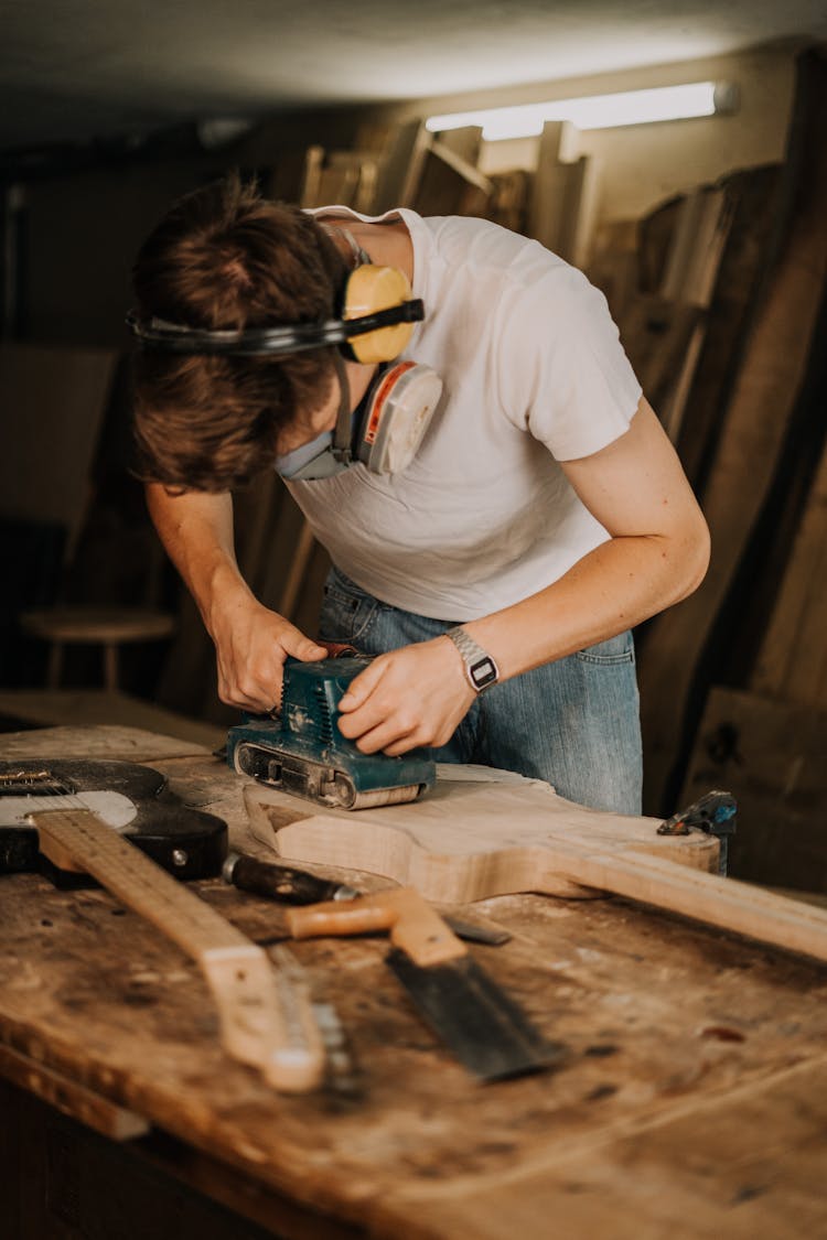 Man In White Shirt Holding A Wood Sanding Machine 