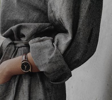 Close-up of a person's arm wearing a classic watch and a textured grey jacket, showcasing elegance.