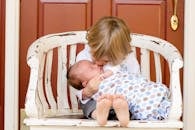 Boy Carrying and Kissing Baby Sitting on Chair