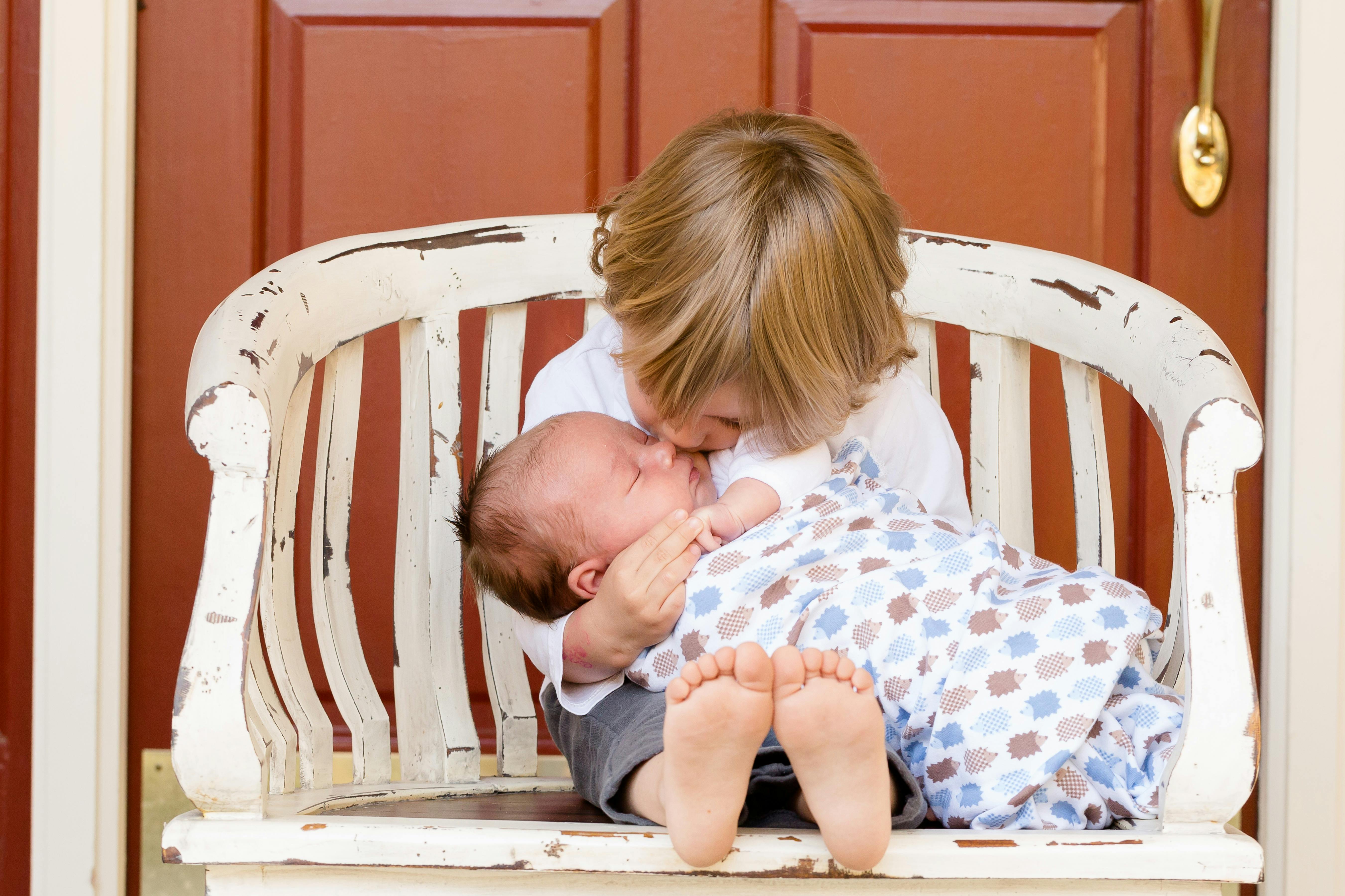 椅子に座っている赤ちゃんを運んでキスする男の子 無料の写真素材