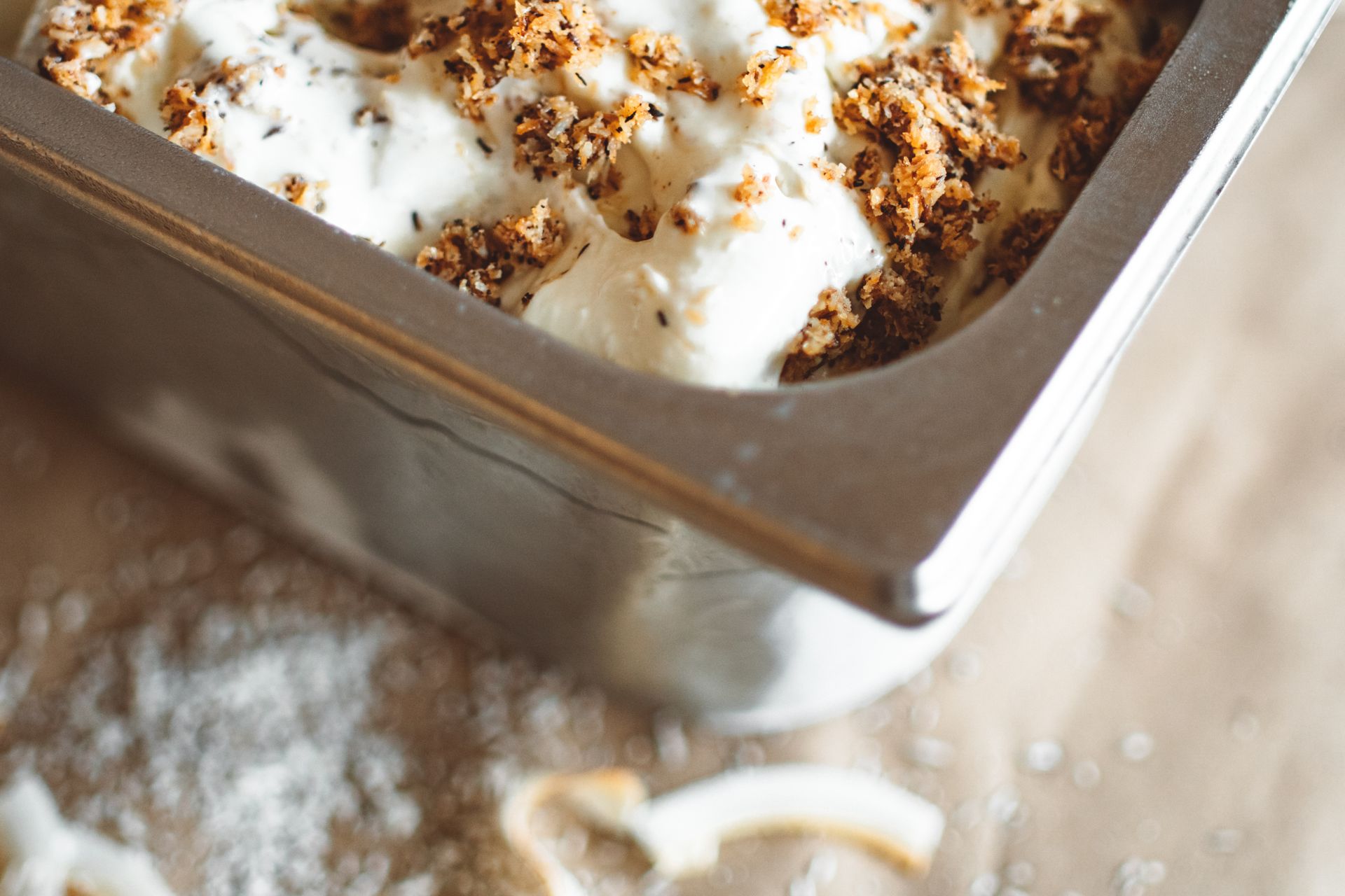 Gourmet ice cream topped with toasted coconut in a metal container. Perfect for dessert lovers.