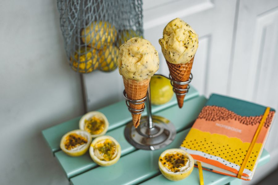 Top view of passion fruit ice cream cones with fresh fruit and a notebook on a table.