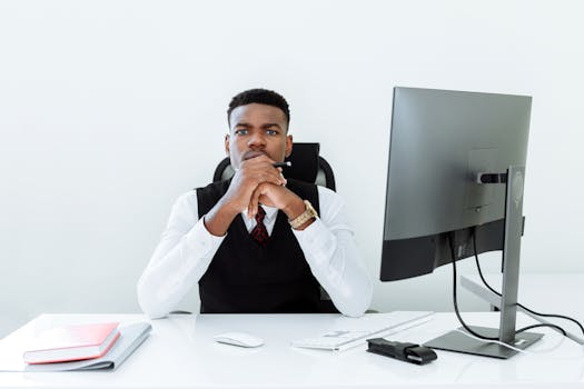 Focused man in business attire at office desk with computer and notepad.