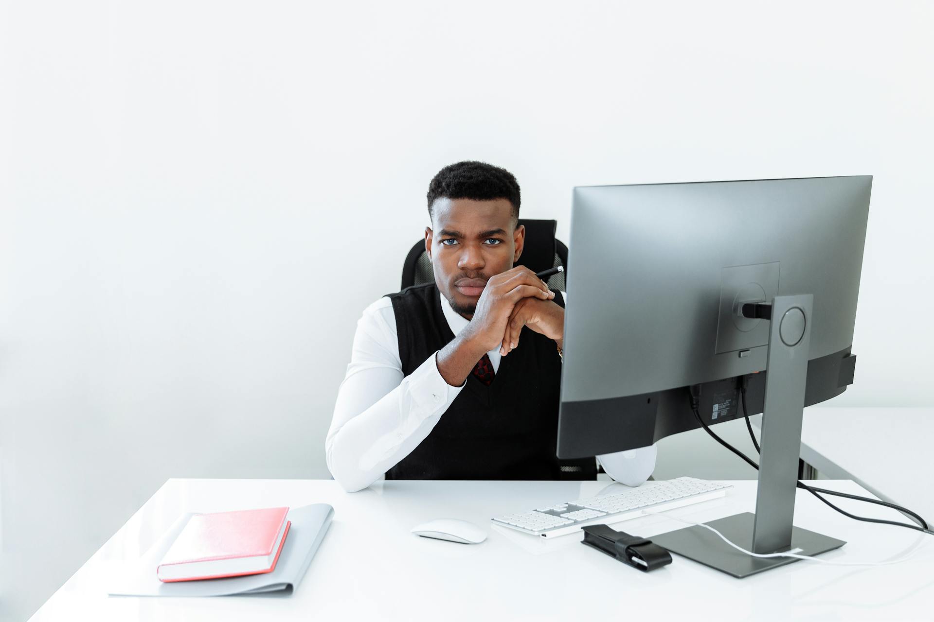 A confident businessman working at a desk with a computer monitor in a minimalist office.