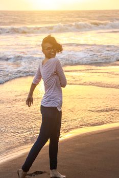 Woman walking barefoot on a sandy beach at sunset, enjoying the ocean breeze.