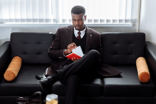 A business professional sits on a couch reading a notebook in an office setting, showcasing focus and productivity.