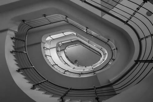 From below black and white of spiral stairway with metal railings  leading up in modern building