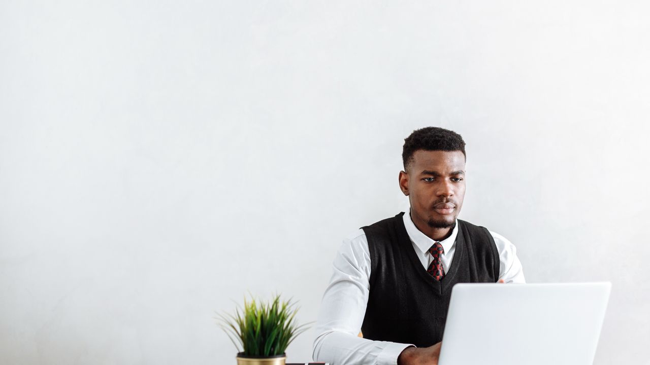 Professional man sitting at a desk working on a laptop in a modern office environment.