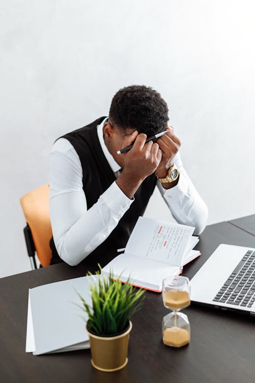 Man in White Dress Shirt Sitting on Chair in Front of Table With Macbook Pro